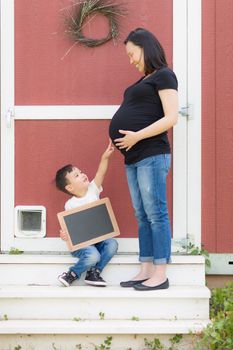 Young Mixed Race Son with Blank Chalk Board Pointing to Pregnant Belly of Mommy