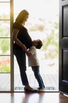 Loving Young Son Hugging Pregnant Mom in Doorway.