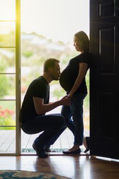 Loving Husband Kissing Belly of Pregnant Wife In Doorway.