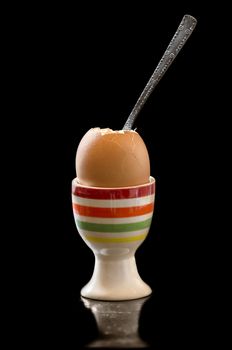 A boiled egg in the stand and spoon on a black background.The reflection on the surface