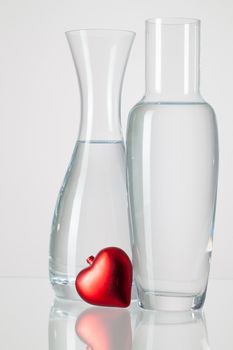 Two vases with clean water and red heart  on a glass table