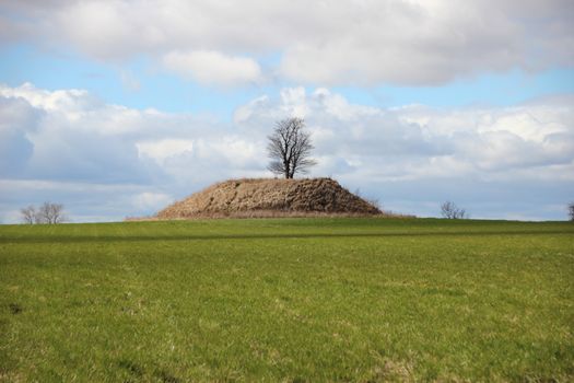 Ancient Burial Mound with Dramatic Clouds and Fresh Green Field