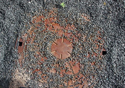 Rusty Sewer Cover Background with Grey Stone Rubble on Top