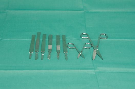 Many types of stainless scalpel and scissors were placed on green fabric.