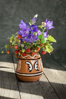 Flowers and strawberries, a small bunch. In a ceramic vase, on the old boards and the grey background.