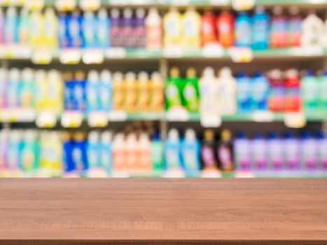Wooden board empty table in front of blurred background. Perspective dark wood over blur colorful supermarket products on shelves. Mock up for display or montage of product