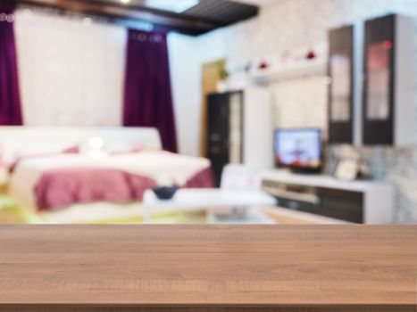 Wooden board empty table in front of blurred background. Perspective dark wood over blur in modern comfortable bedroom with beige bed