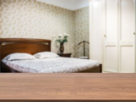 Wooden board empty table in front of blurred background. Perspective dark wood over blur in modern comfortable bedroom with dark brown wooden bed. Mock up for display or montage your products