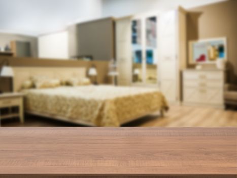 Wooden board empty table in front of blurred background. Perspective dark wood over blur in modern comfortable bedroom with beige bed. Mock up for display or montage your products