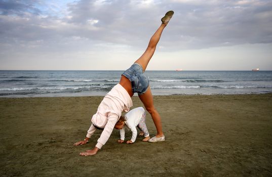 Young woman with small douther practicing yoga on the sea beach at sunset