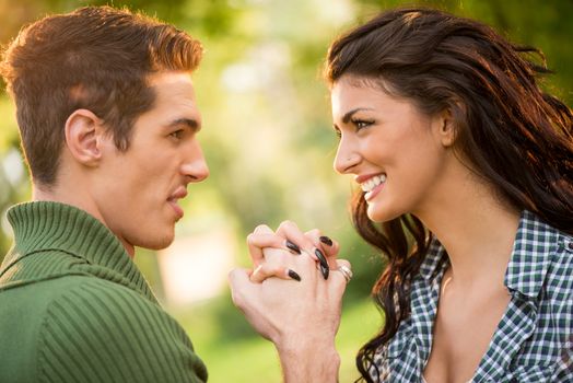 Close-up of a young heterosexual couple, holding hands facing each other and look at each other with a smile.