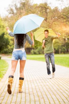 Meeting of young girl and a guy in the park, while holding umbrellas rushing into each other's arms.