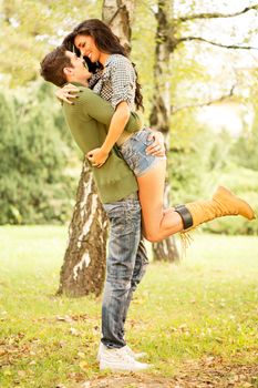 Embrace the young loving couple in the park. The guy rising hot girlfriend in height in a passionate embrace.