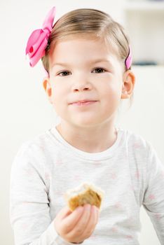 Little cute smiling girl with hair clip, holding a delicious pastry and looking at the camera.