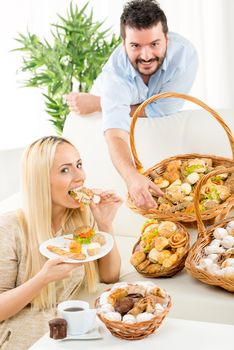 Beautiful blonde girl and a guy with a beard, eat pastries. Beside them are woven baskets full of salty and sweet pastries.