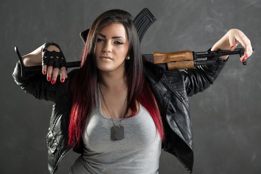 Attractive young woman with an automatic rifle standing with hands leaning on the rifle that was put behind the neck. With a dangerous expression on her face looking at the camera.