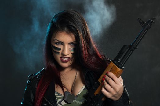 Attractive brunette with an automatic rifle, with war paint on her face and a dangerous expression with clenched teeth, looking at the camera.