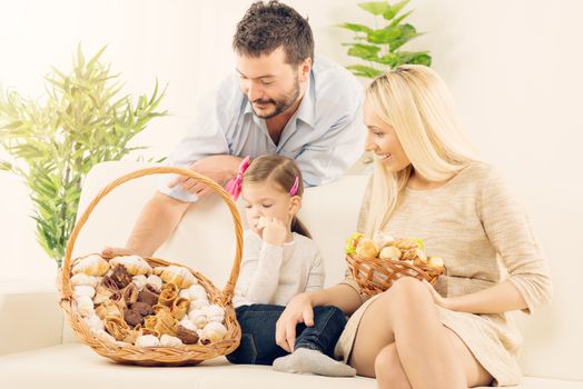 Young man leaning against the couch on which sat his cute daughter and beautiful wife, holding a wicker basket with pastries glad that his will have breakfast with family.