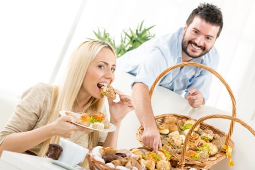 Beautiful blonde girl and a guy with a beard, eat pastries. Beside them are woven baskets full of salty and sweet pastries.