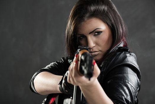 Attractive girl standing in the attitude of aiming and looking through the sight automatic rifle, which is directed towards the camera.