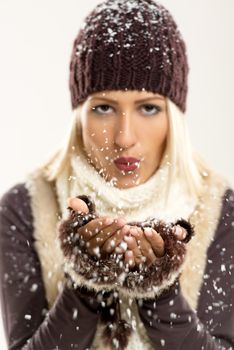 Beautiful young blonde girl In winter clothes, blowing snowflakes In the viewer. The focus is on the hands with snow.