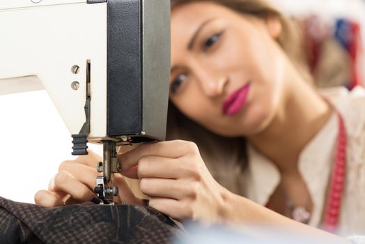 Close-up sewing machine and hand of a young woman, whose face is out of focus while doing a fine job of needle on sewing machine.