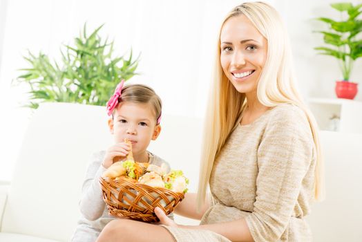 Beautiful smiling mother gives a wicker basket with fresh pastries her daughter, who gladly eat mom's pastry.