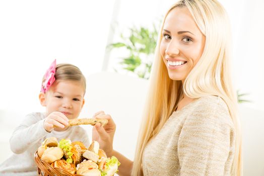 Beautiful mother gives a wicker basket with fresh  bakery products her daughter. With a smile looking at the camera.