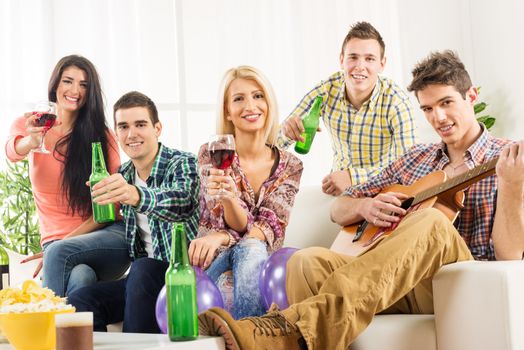 Cheerful friends at home party toasting with bottles and glasses. With a smile looking at the camera.