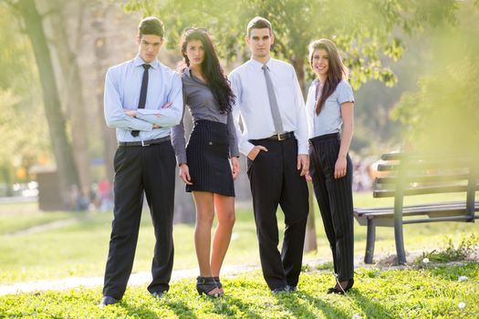 Small group of business people, elegantly dressed, standing in the park,enjoying the sunny day, looking at the camera.