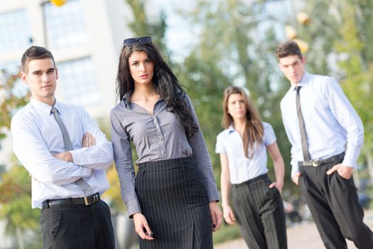 Group of young business people elegantly dressed standing outside enjoying the beautiful day, with a serious expression on their faces looking at the camera.