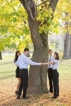 Group of young business people standing in a park hugging a tree trunk. With a smile on their faces looking at the camera.