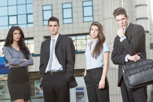 Group of young successful business people standing in front of office building dressed in suits. With a serious expression on their faces looking at the camera.