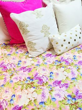 Bed with colorful floral design bedclothes and lots of pillows.
