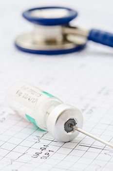 medical ampoules and needle with stethoscope on cardiogram.