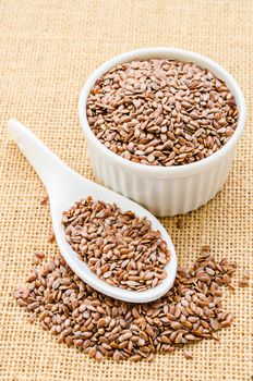 Brown flax seeds or linseeds in a spoon on sack background.