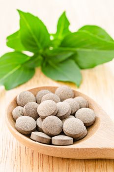 Medicine herb drug in wooden spoon with green leaf on wooden table.