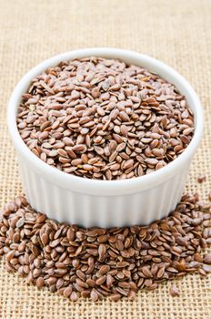 Brown flax seeds or linseeds in white bowl on sack background.