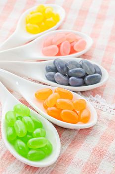 Colorful candies in white spoon on tablecloth background