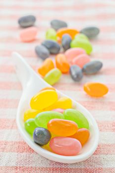 Colorful candies in white spoon on tablecloth background