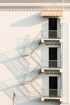 fire escape with afternoon shadows on exterior white wall.