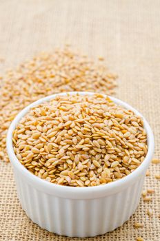 Heap of gold linseed or flax seeds in white cup on sack background, concept for healthy nutrition