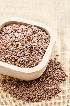 Heap of brown linseed in wooden cup on sack background, concept for healthy nutrition