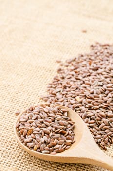 Heap of brown linseed, flax seeds with wooden spoon on sack background, concept for healthy nutrition