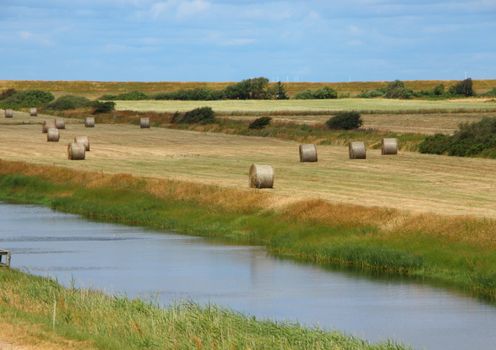 Round Golden Straw Bales in Summer Landscape Field with River