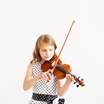 Portrait of girl with string and playing violin. Portrait of the little violinist. Beautiful gifted little girl playing on violin against the white background