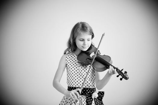 Portrait of girl with string and playing violin. Portrait of the little violinist. Beautiful gifted little girl playing on violin against the white background