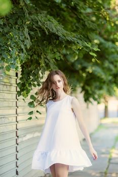 Portrait of lovely urban girl in short white dress in the street. Portrait of a happy smiling woman. Fashionable blonde girl having fun outdoors in the city