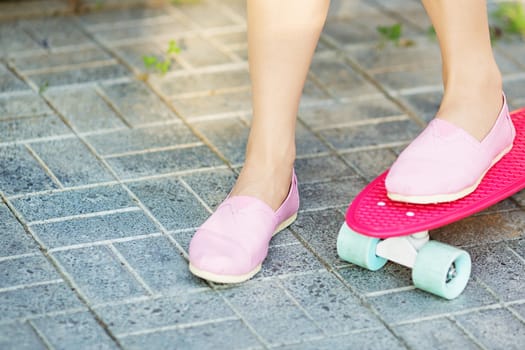 Girl standing on a pink skateboard outdoors. Closeup image of female feet at skateboard. Female feet in sneakers on a pink skateboard. Girl rides on the asphalt on a plastic skateboard