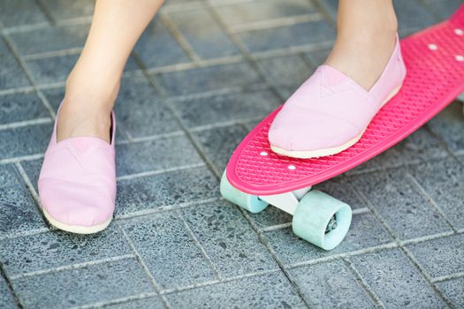 Close up of feet of beautiful girl in pink sneakers rides on pink penny skate board with blue wheels. Urban scene, city life. Sport, fitness lifestyle. Cute hipster have fun.